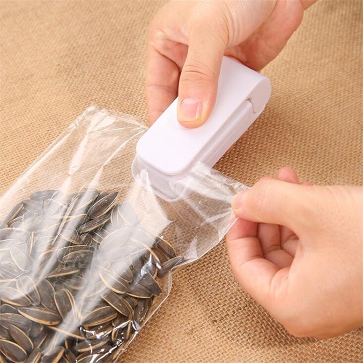 Fourfold Pinch handheld bag sealer being slid along the top of an open bag of sunflower seeds