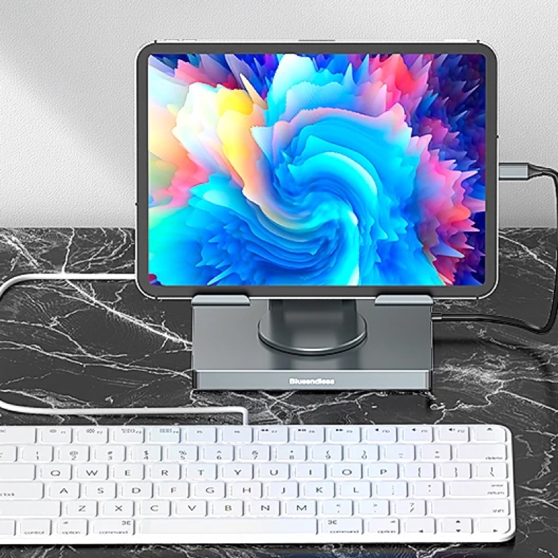 Fourfold 360 Tablet Stand & Hub holding a tablet upright on a marble desk, a white keyboard in front of it